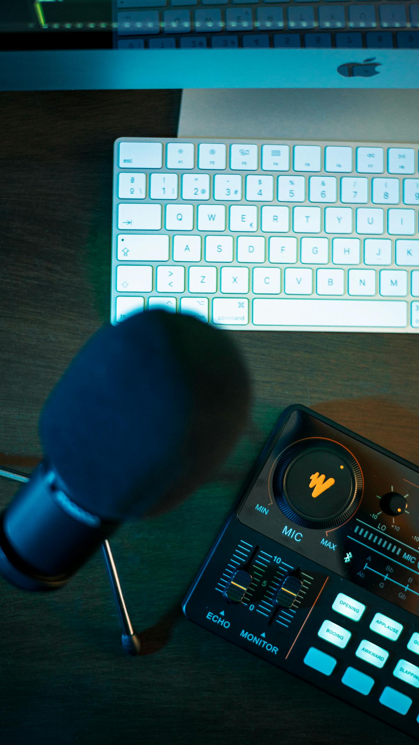 A sleek podcasting setup featuring a microphone, audio control panel, and keyboard.