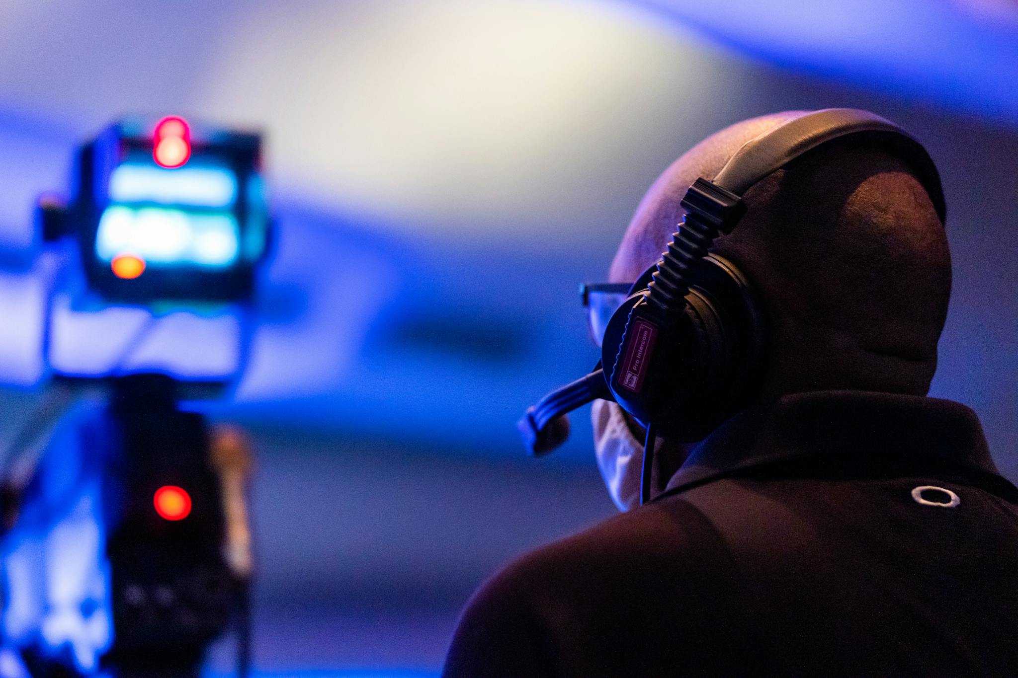 A bald man with a headset overseeing a live event in a dimly lit environment with a blurred camera in the foreground.